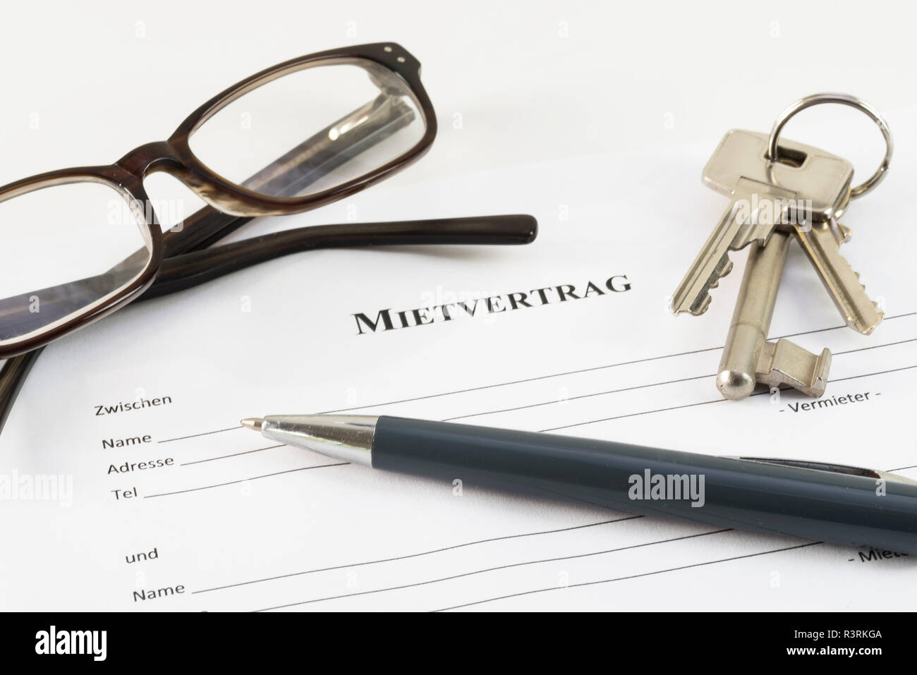 German lease agreement document with house keys,  glasses and a ball pen, Mietvertrag means rental contract, selected focus, narrow depth of field Stock Photo