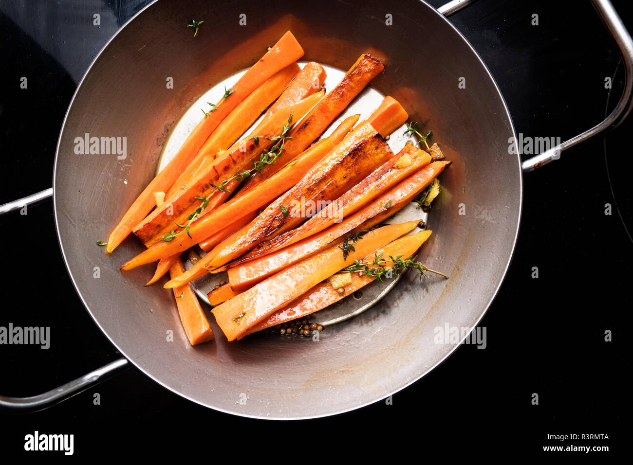 root vegetables, glazed carrots with thyme, ginger and honey in an iron pan on the black stove, high angle view from above Stock Photo