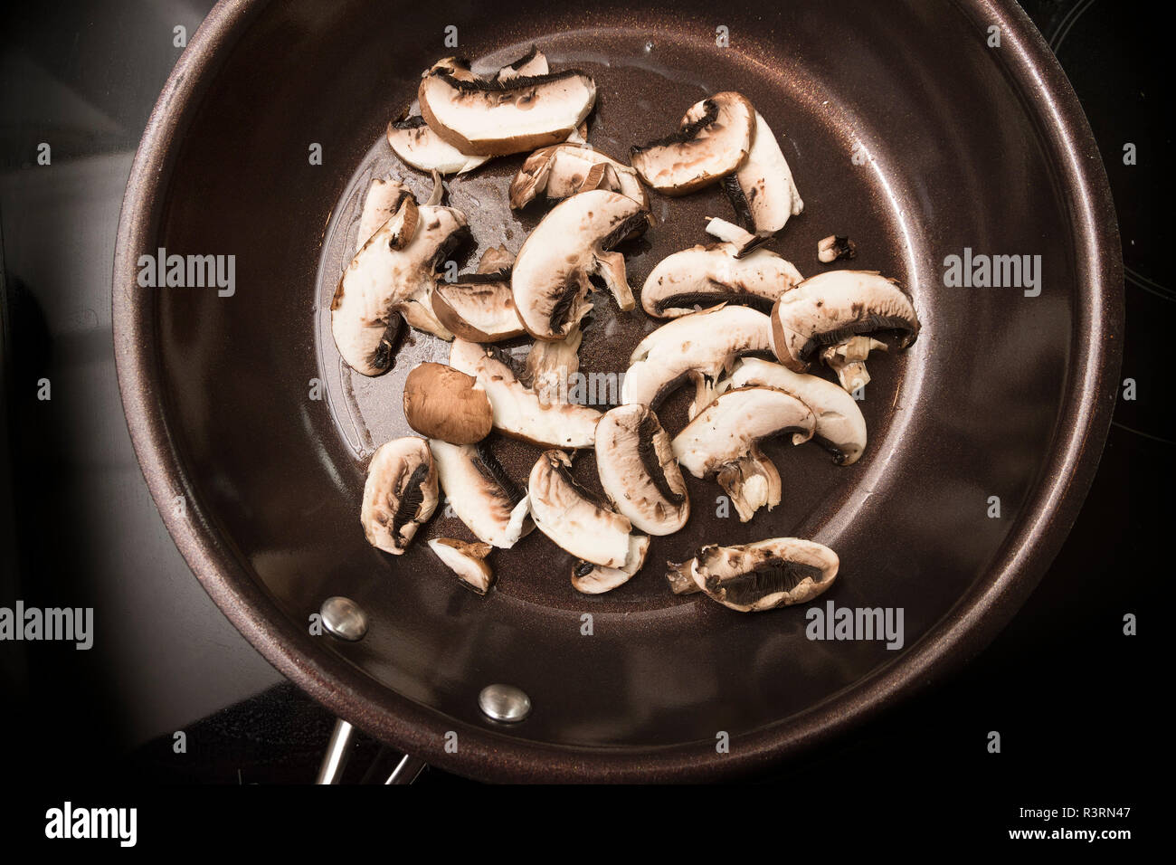 mushroom slices are fried in a cooking pan on the black stove, high angle view from above Stock Photo