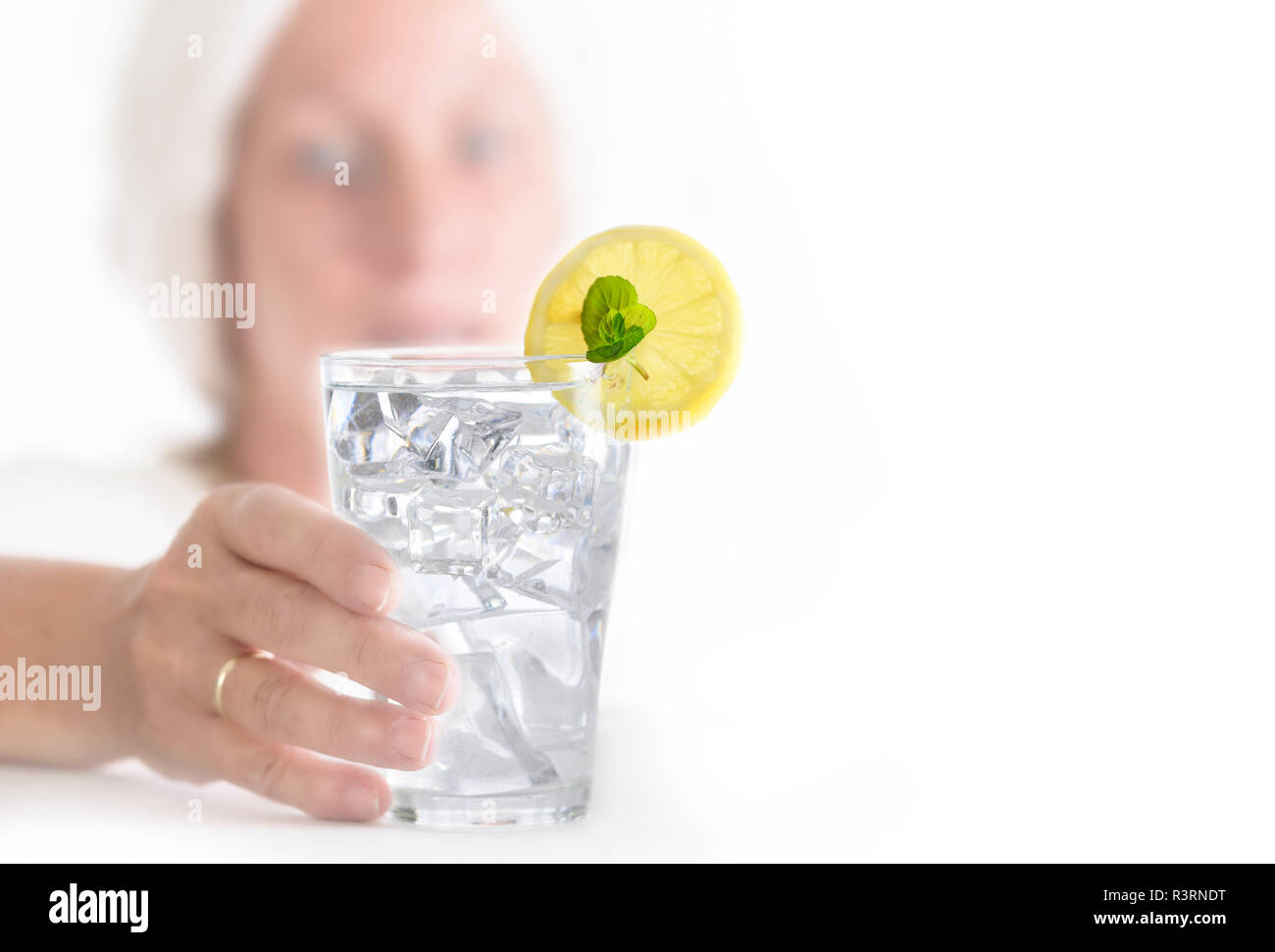woman with blurred face reaches for a glass of water with ice cubes and lemon slice, white background with copy space, selected focus, narrow depth of Stock Photo