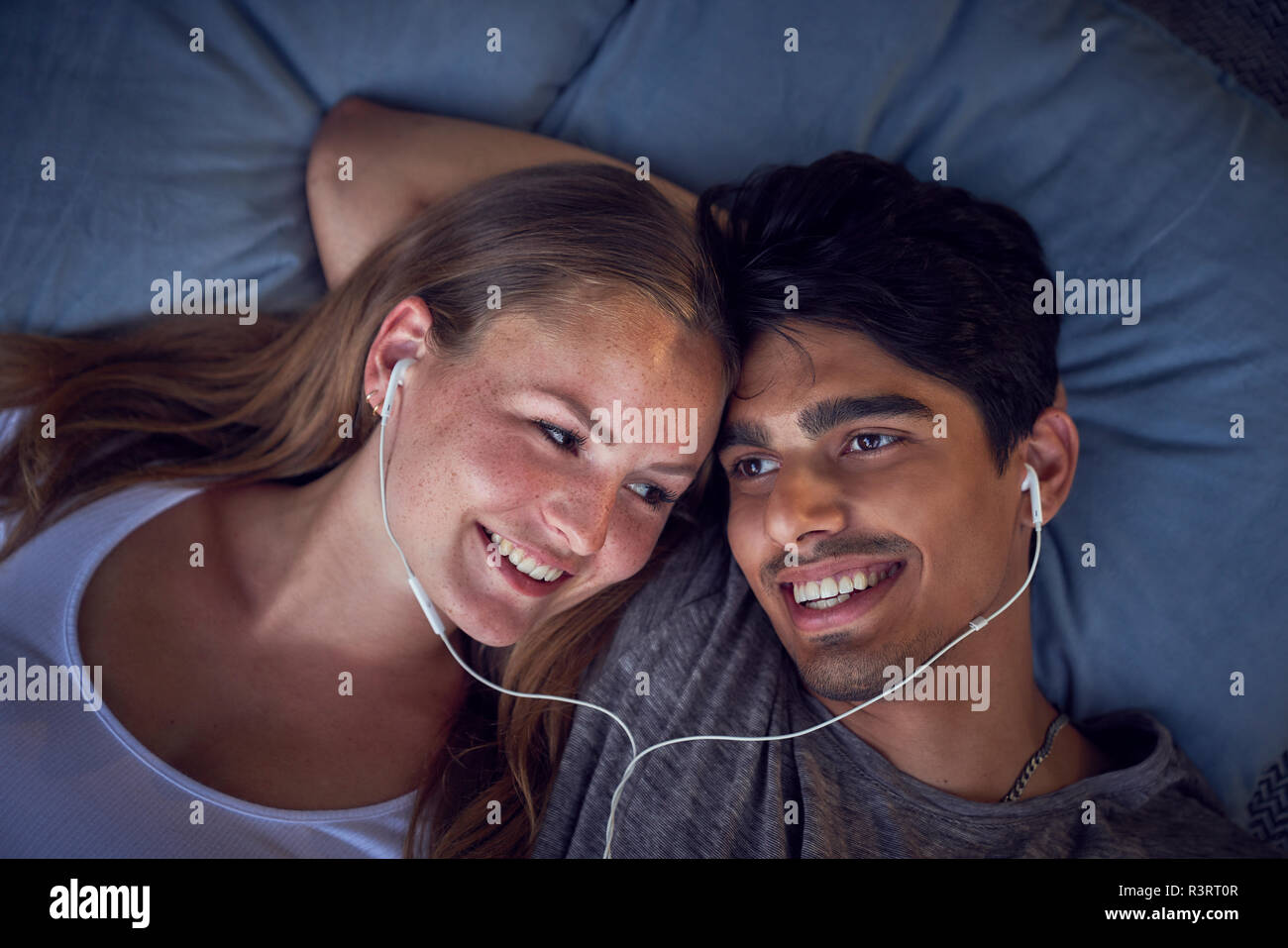 Young couple lying on cushions, sharing earphones, listening music Stock Photo
