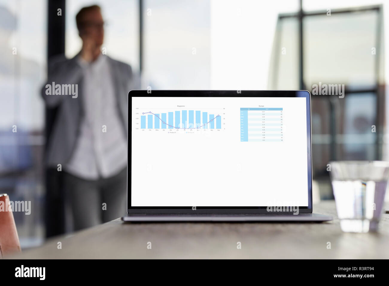 Chart on laptop screen on desk in office with businessman in background Stock Photo