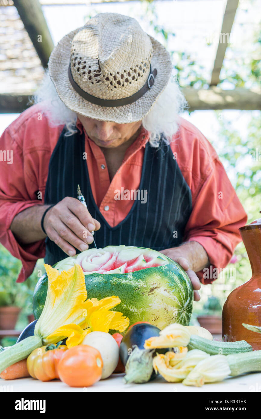 Senior man working on a watermelon with carving tool Stock Photo