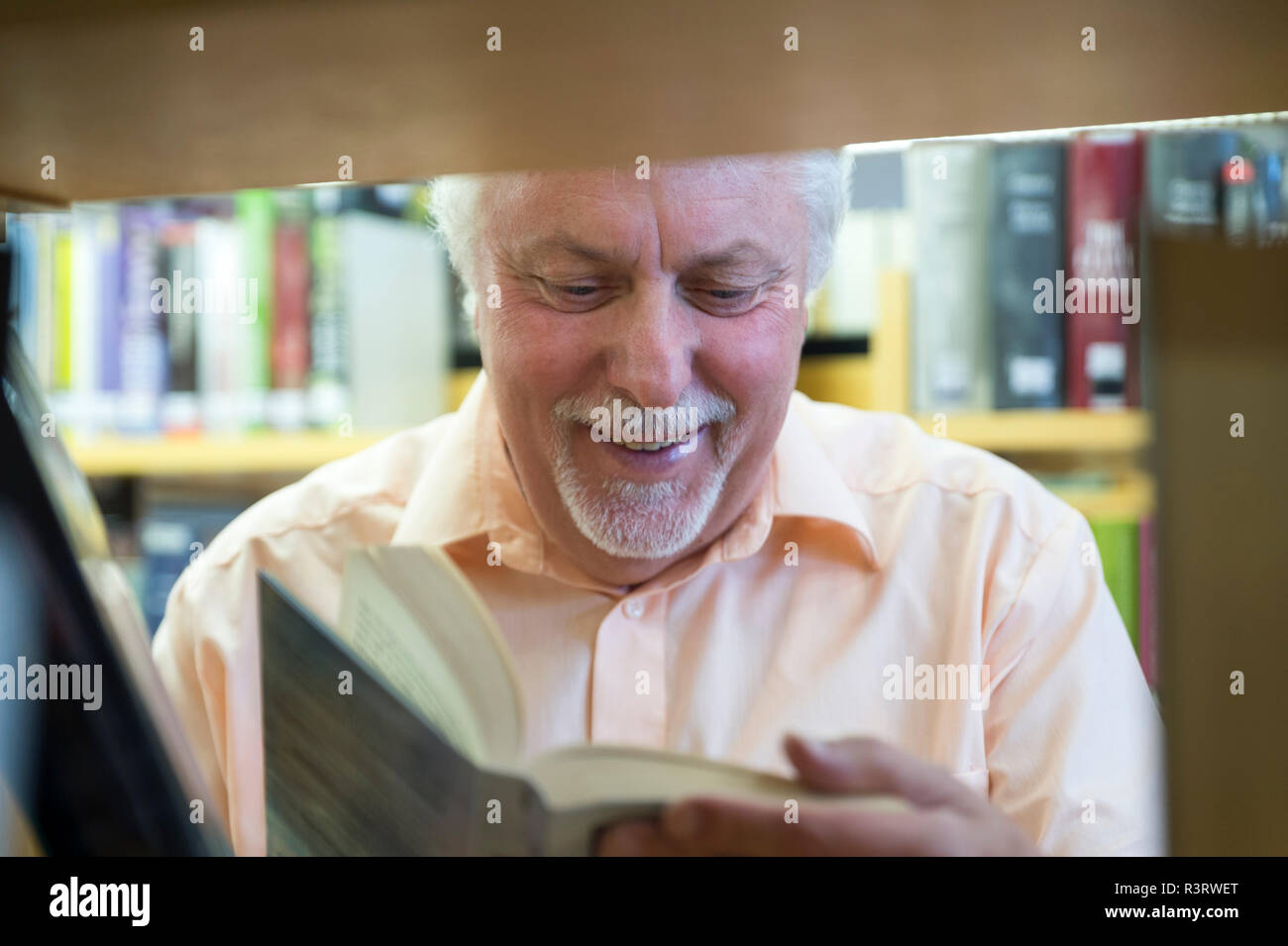 Senior liest lachen ein Buch an einem BÃ¼cherregal. Grevenbroich, Nordrhein-Westfalen, Deutschland Stock Photo