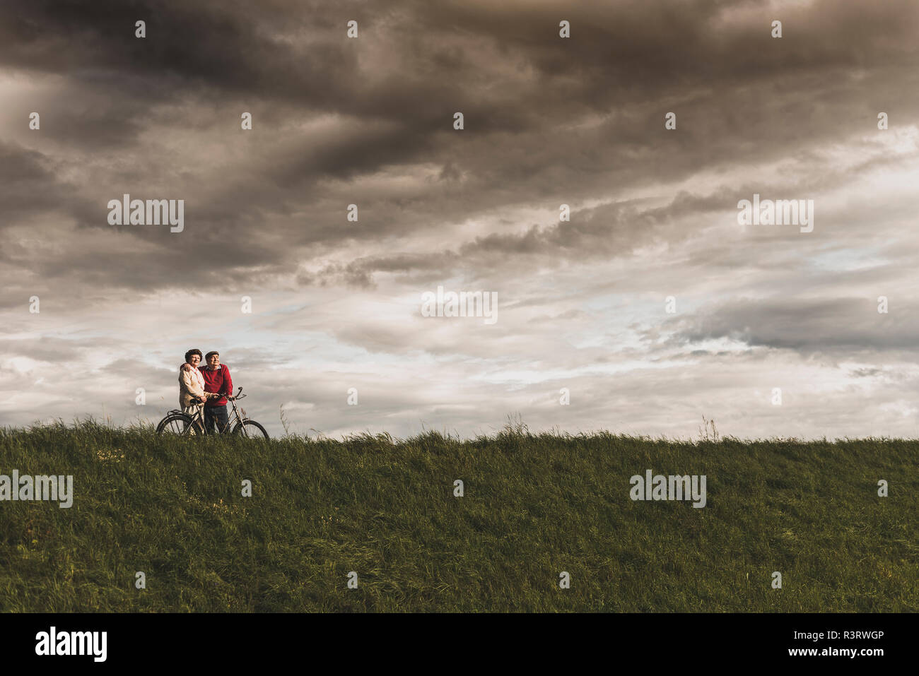Senior couple with bicycles in rural landscape under cloudy sky Stock Photo