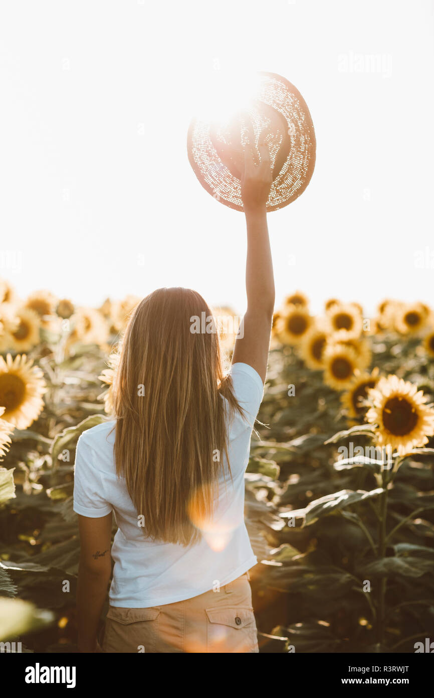 Back view of young woman holding straw hat, standing in a field of ...