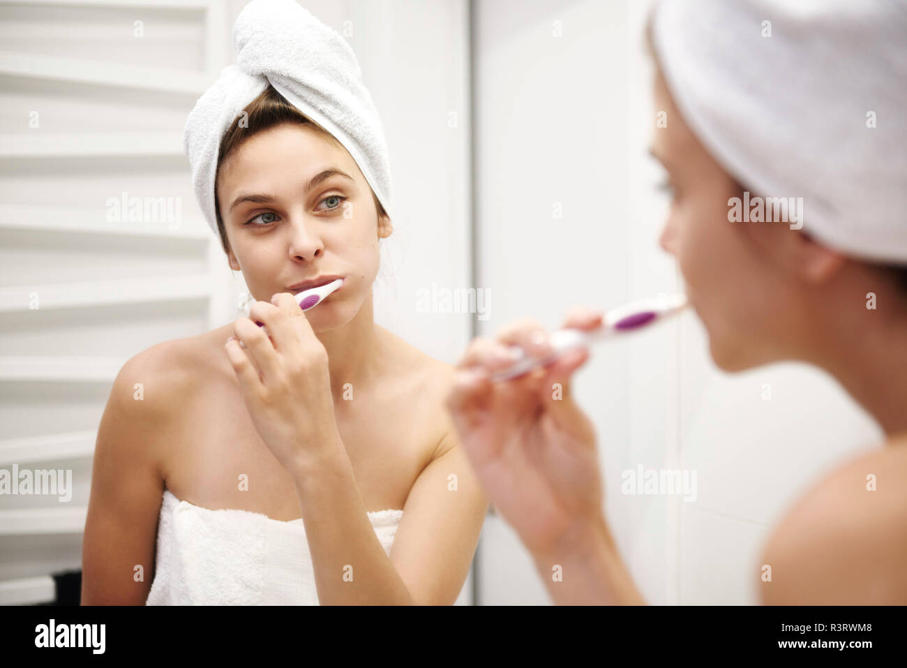 Mirror image of young woman in bathroom brushing her teeth Stock Photo