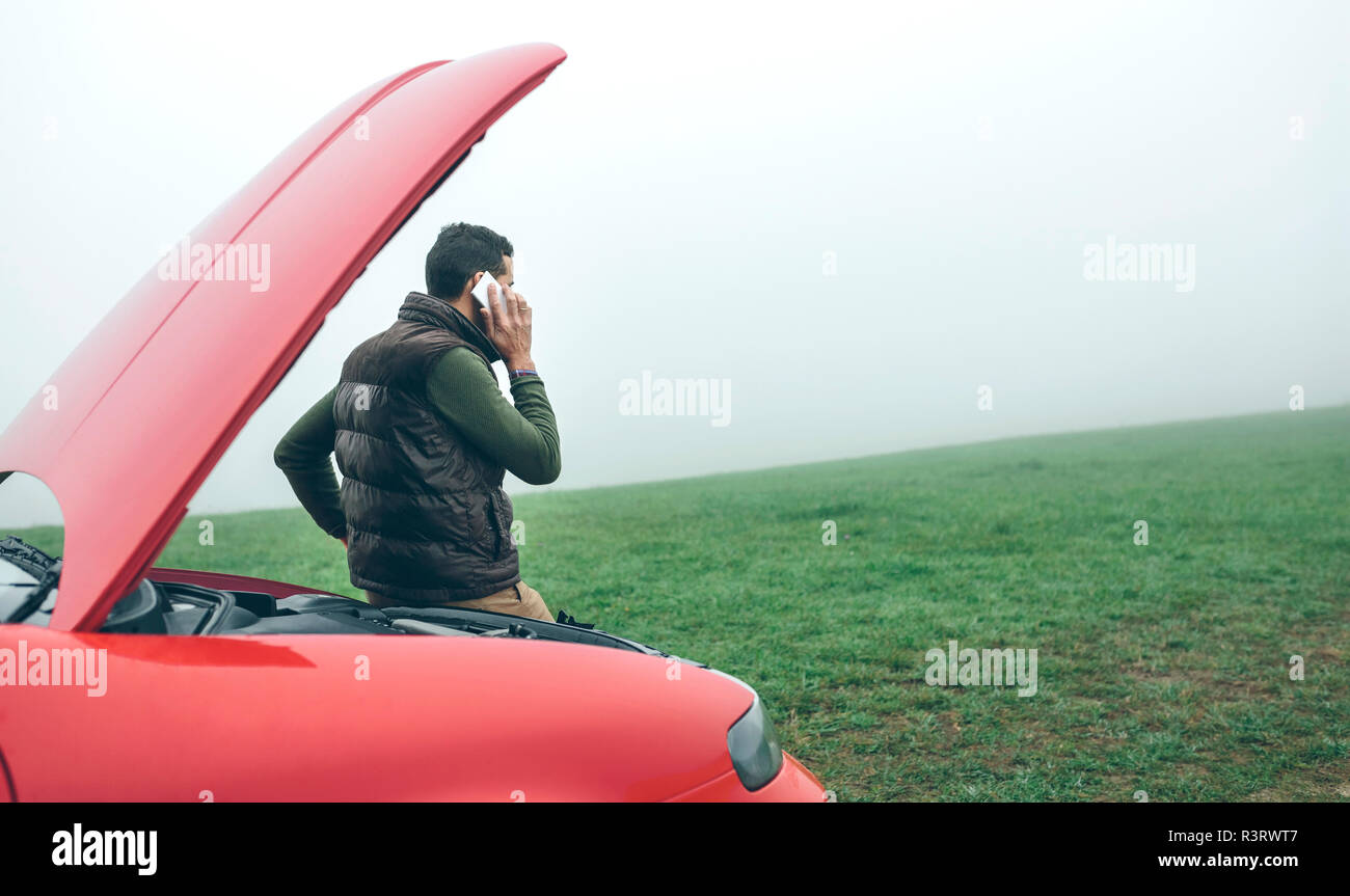 Man talking on cell phone next to broken car Stock Photo