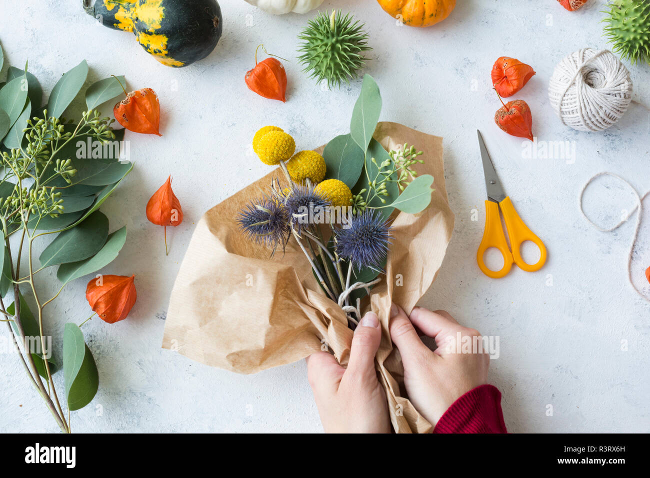 Autumnal decoration, ornamental pumpkins, hands wrapping bunch of flowers Stock Photo