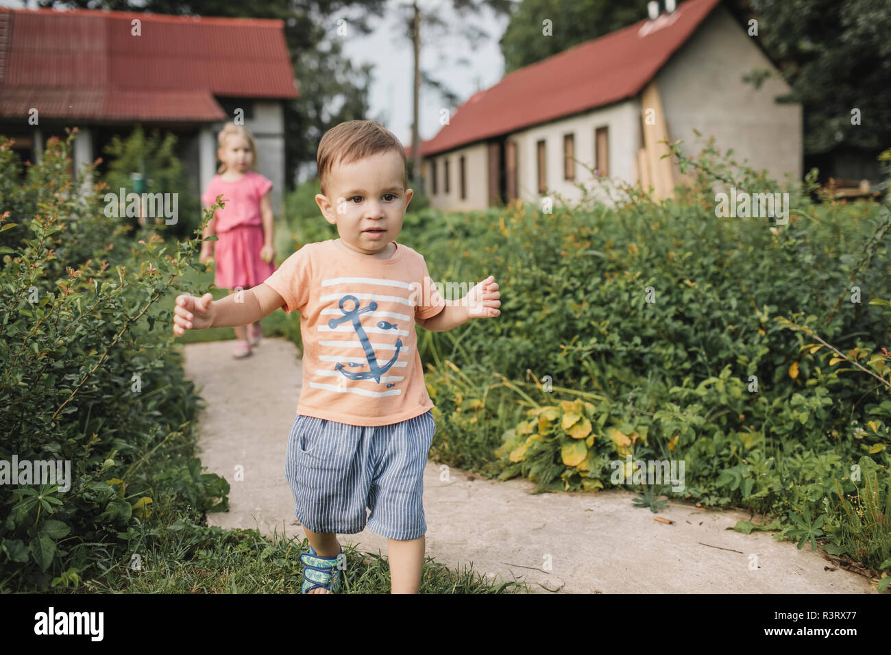 Baby boy walking in garden with sister in background Stock Photo
