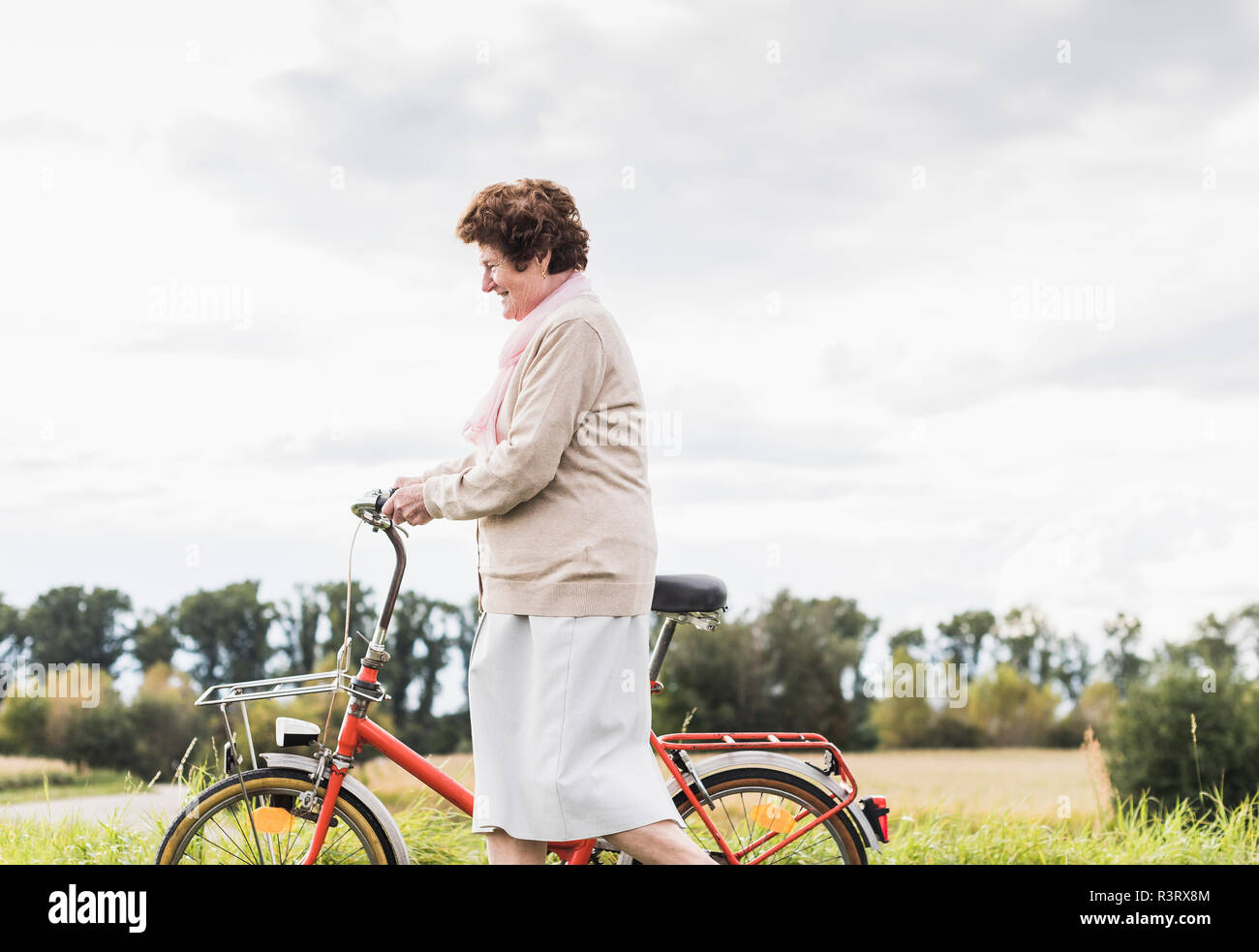 Senior woman pushing bicycle in rural landscape Stock Photo