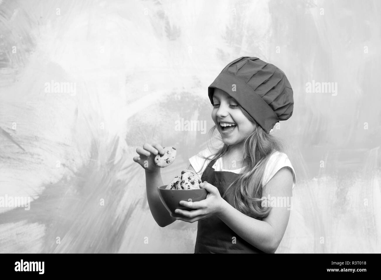 small baby girl or cute child with happy face in red chef hat and cook apron holding bowl with chocolate cookies on colorful abstract background, cook Stock Photo