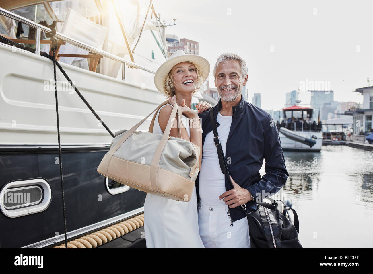 Older man and young woman standing with travelling bags on jetty next to yacht Stock Photo