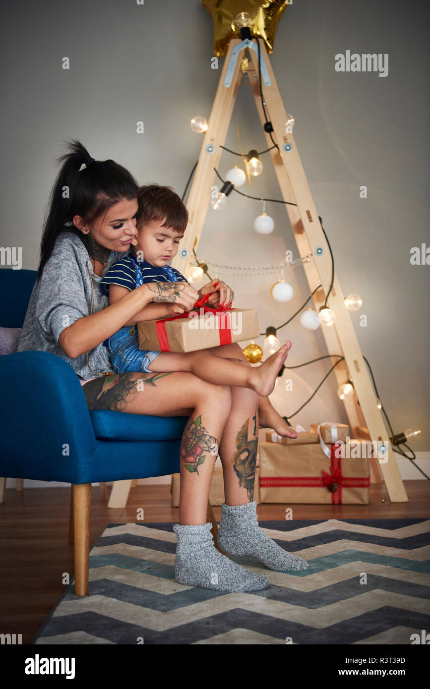 Boy opening Christmas present with his mother at home Stock Photo