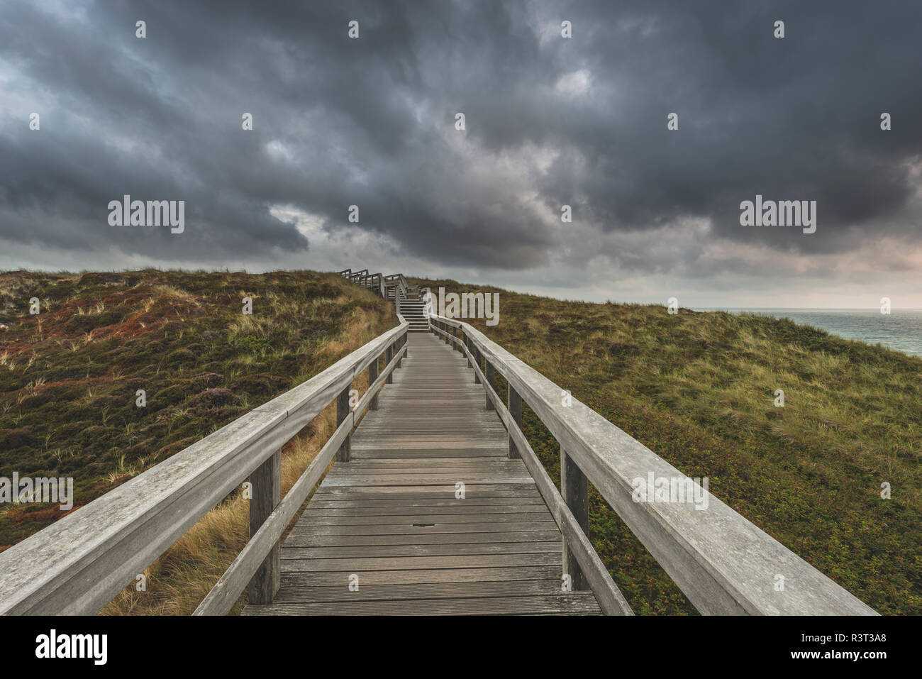 Germany, Schleswig-Holstein, Sylt, Wenningstedt, boardwalk to the beach under rain clouds Stock Photo