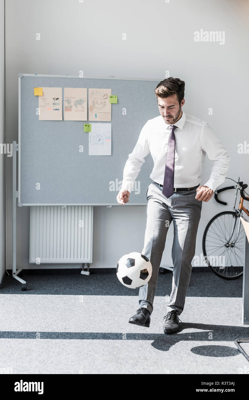 Businessman playing football in office Stock Photo
