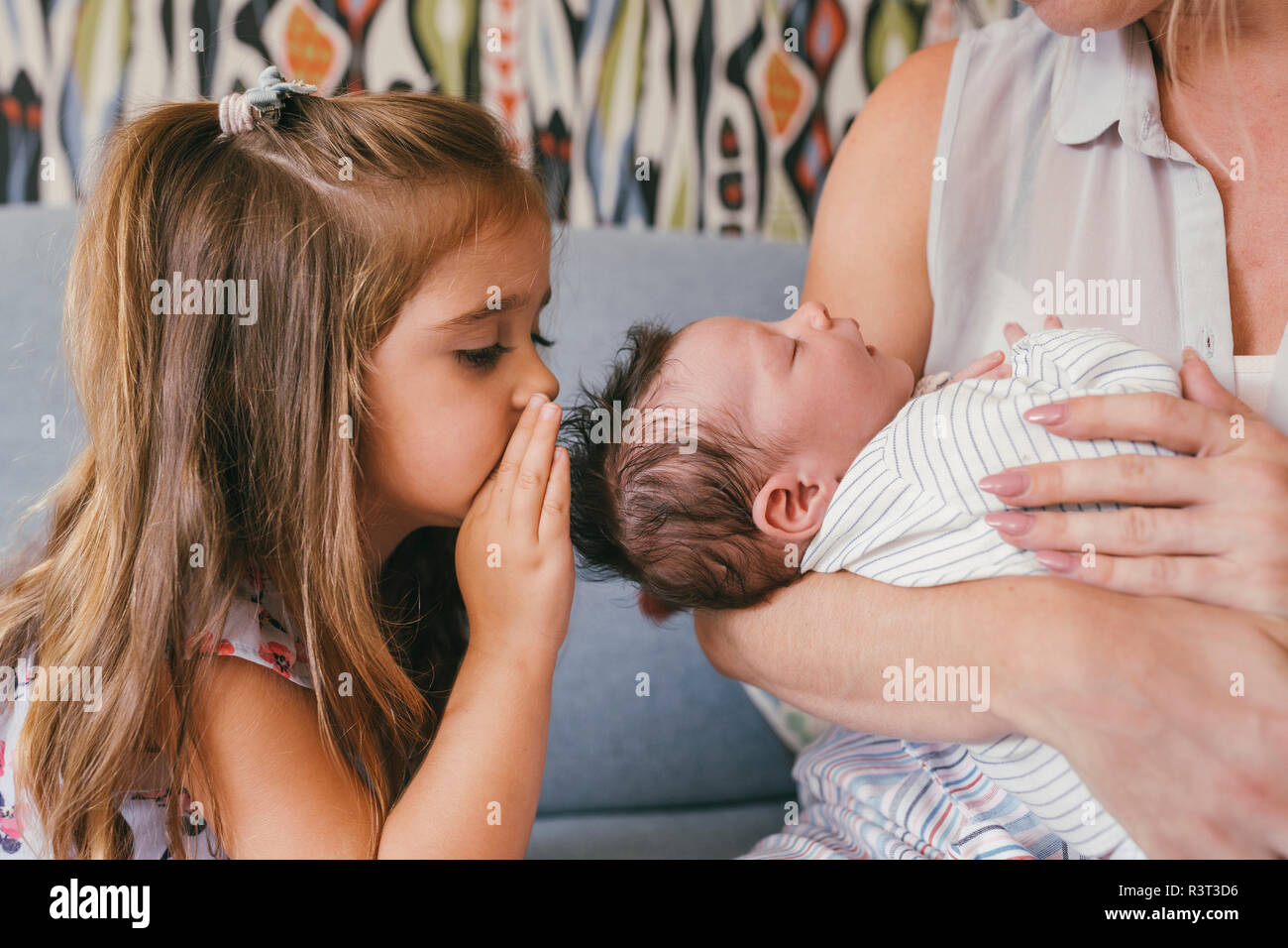 Mother holding her baby close with sister whispering at him Stock Photo