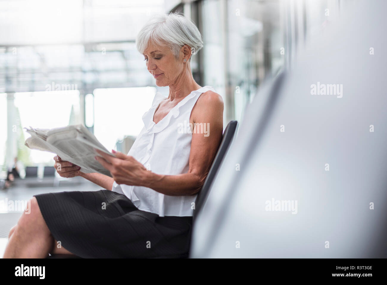 Senior woman sitting in waiting area reading newspaper Stock Photo