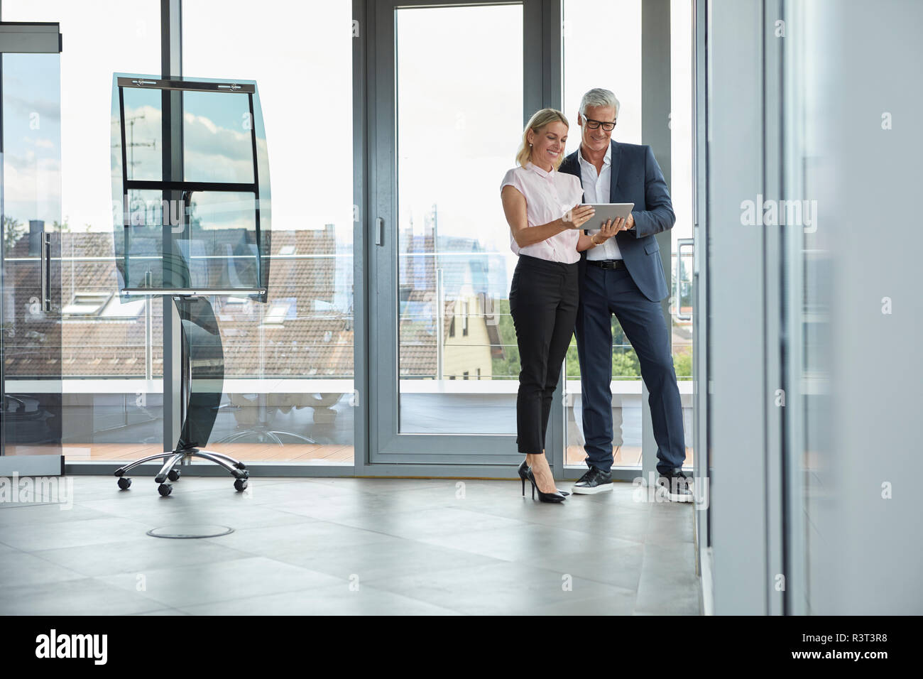 Businessman and woman standing in office, discussing project, looking at digital tabet Stock Photo