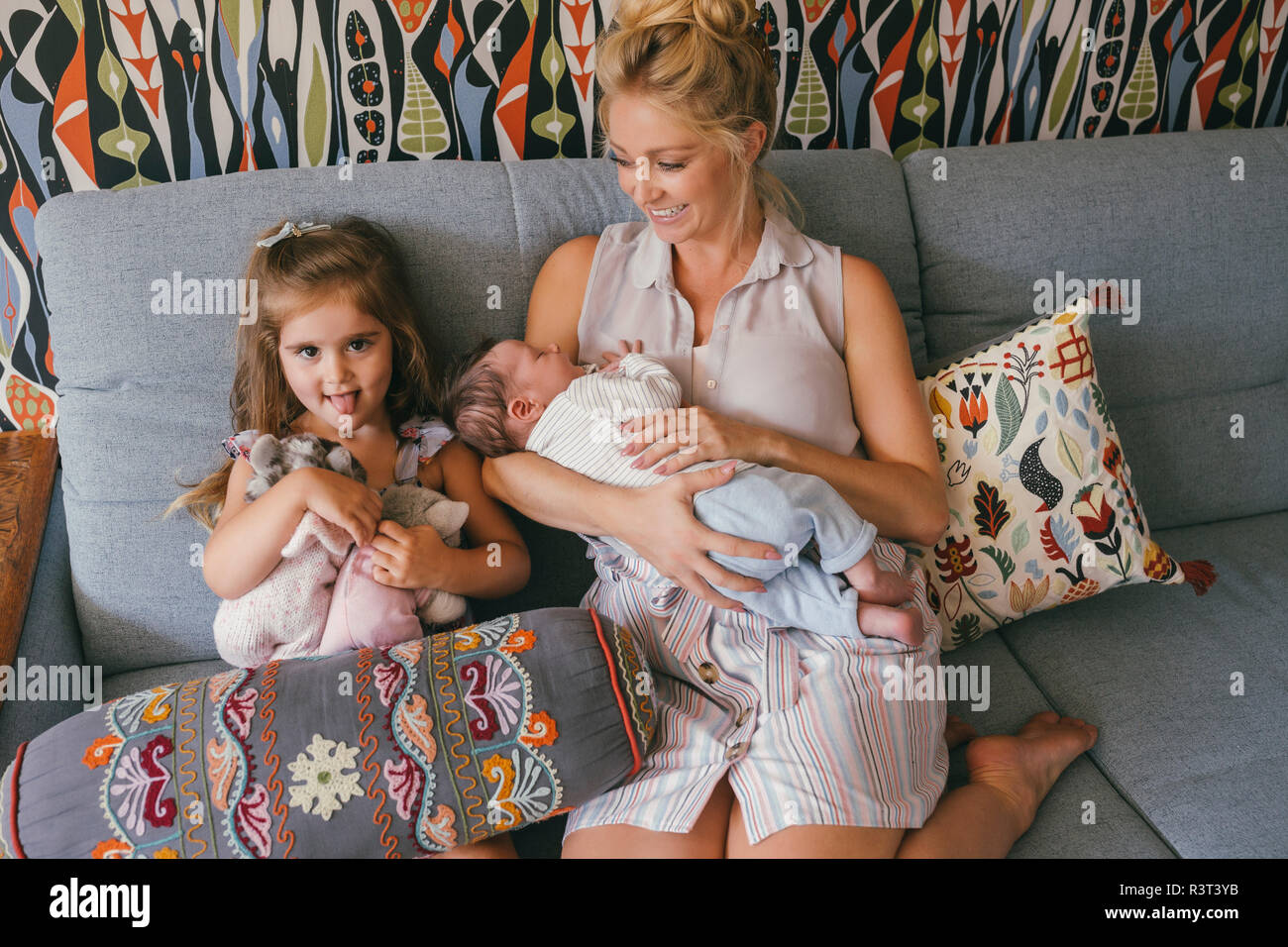 Smiling mother sitting on couch with newborn baby and daughter Stock Photo