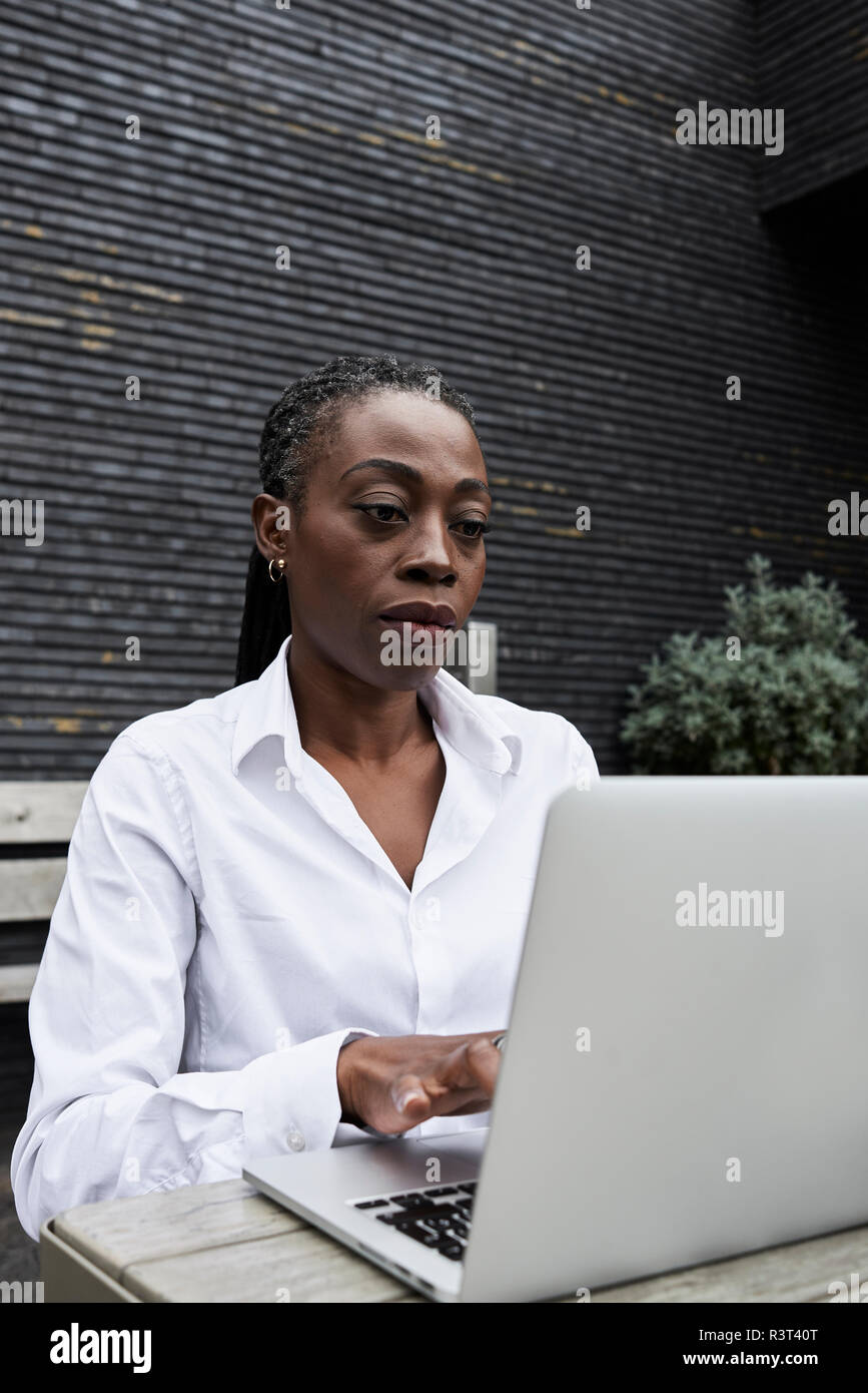 Portrait of businesswoman sitting on  terrace of a coffee shop working on laptop Stock Photo