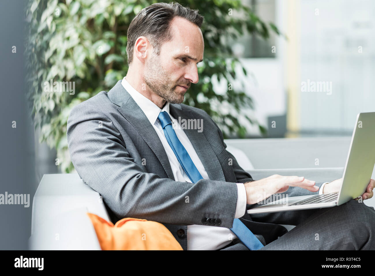 Businessman sitting in lobby using laptop Stock Photo