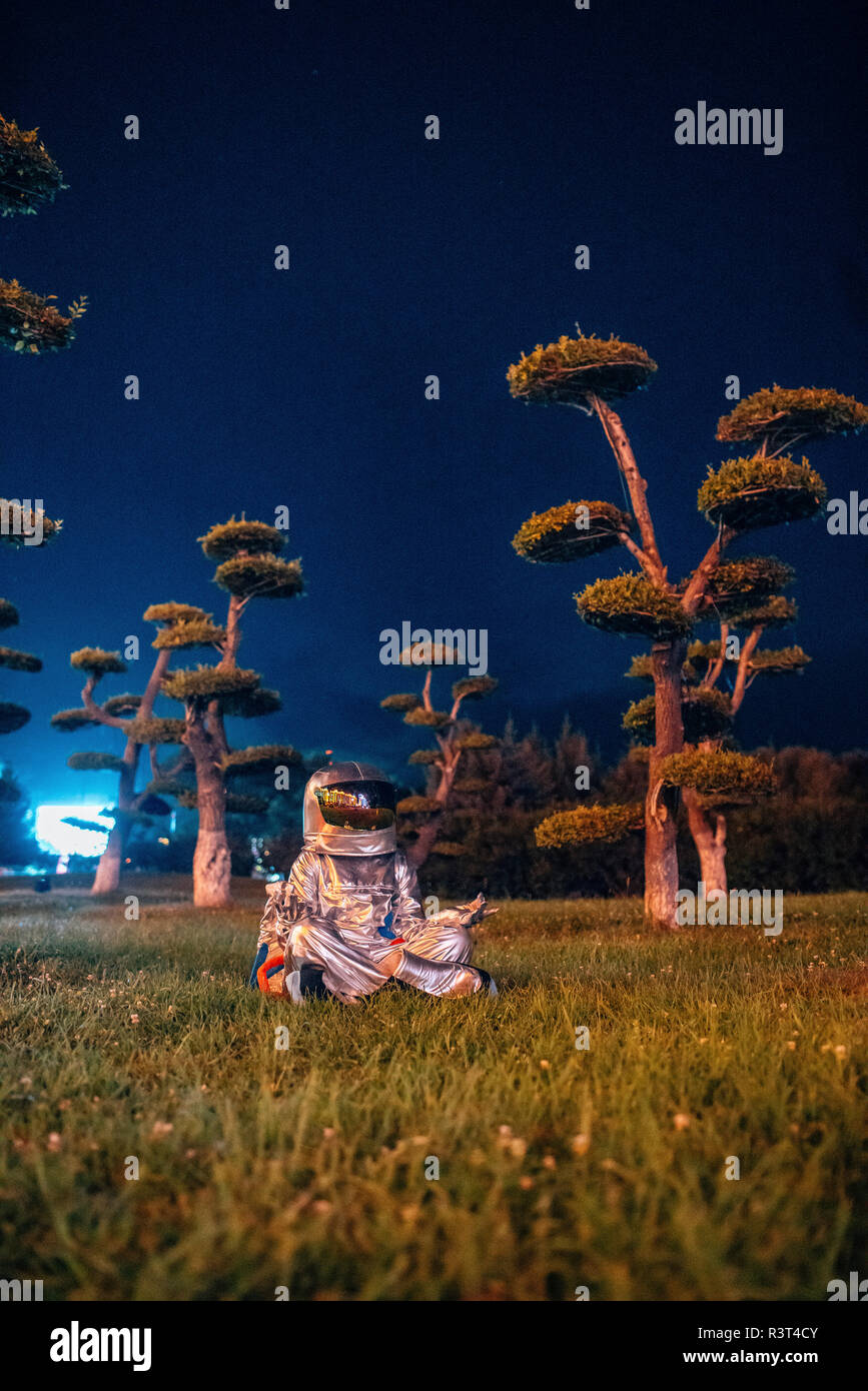 Spaceman in yoga pose siting in a park at night Stock Photo