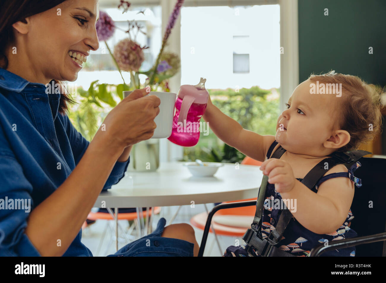 Happy mother and baby daughter clinking coffee cup and baby bottle Stock Photo