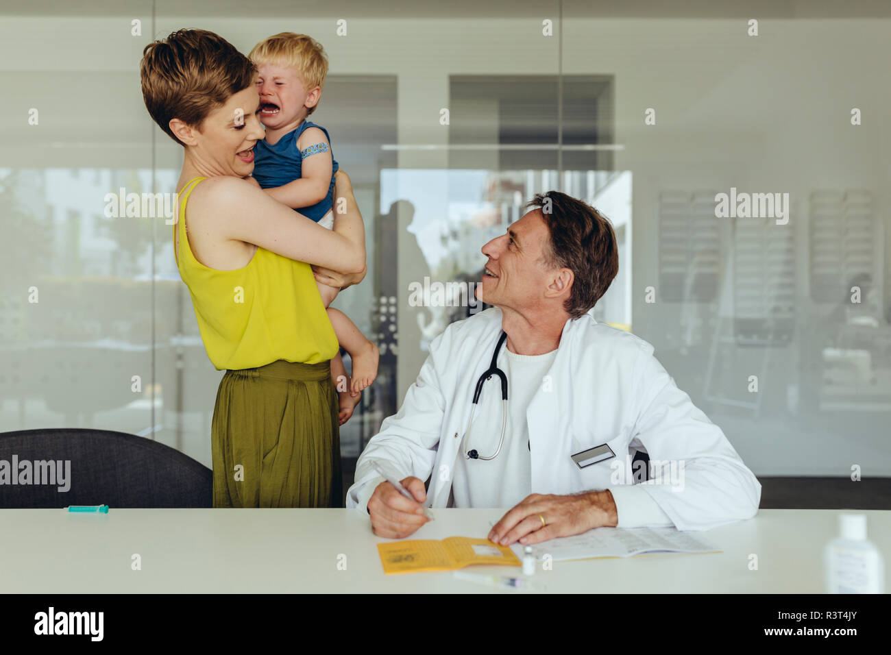 Infant crying in mother’s arms after pediatrician has vaccinated him Stock Photo