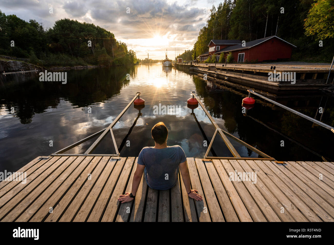 Finland, Kajaani, Man sitting on jetty, watching sunset, rear view Stock Photo