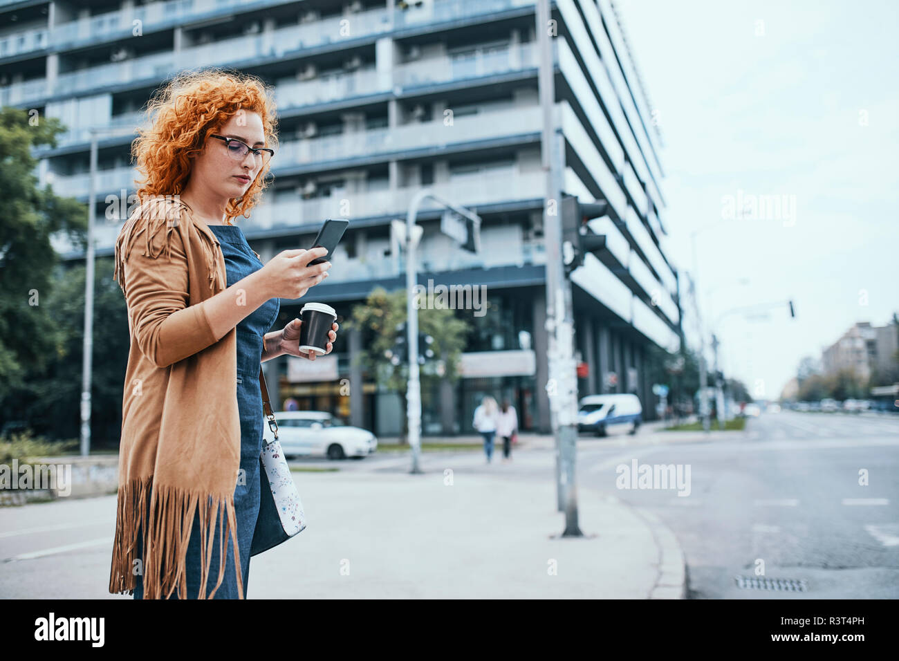 Young woman waiting to cross road, using smartphone Stock Photo