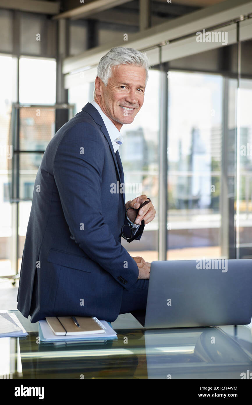 Successful manager sitting on desk, smiling Stock Photo