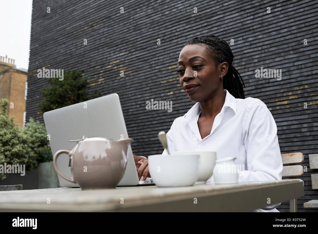 Portrait of smiling businesswoman sitting on terrace of a coffee shop working on laptop Stock Photo