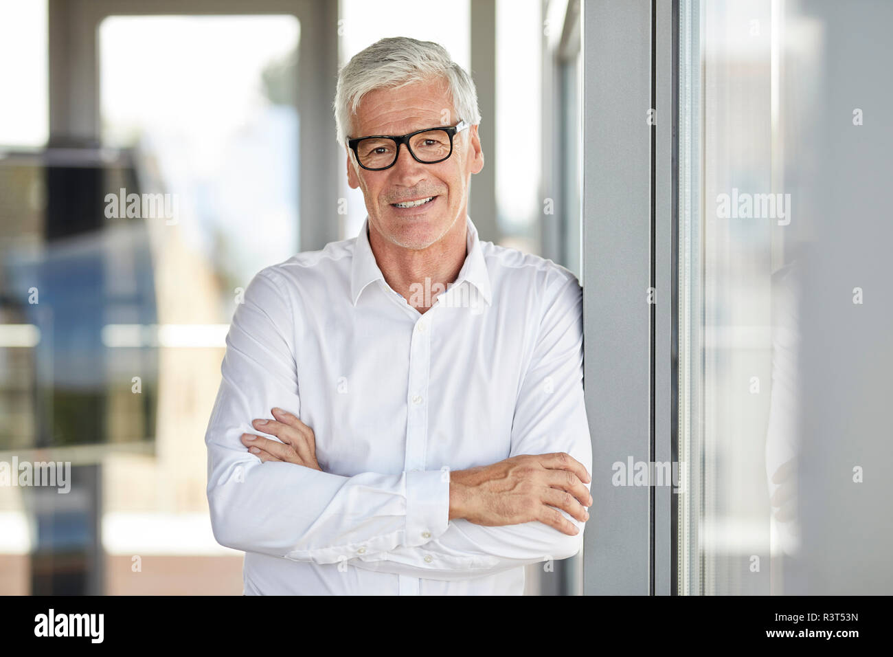 Businessman in office leaning against window, with arms crossed Stock Photo