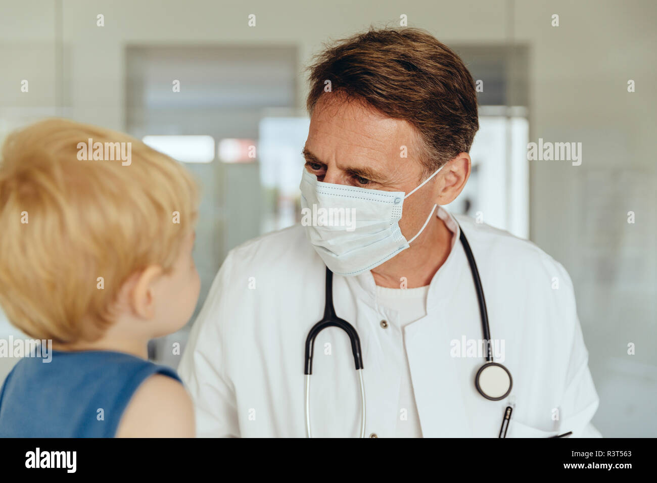 Toddler sitting on lap of pediatrician, wearing protective mask Stock Photo