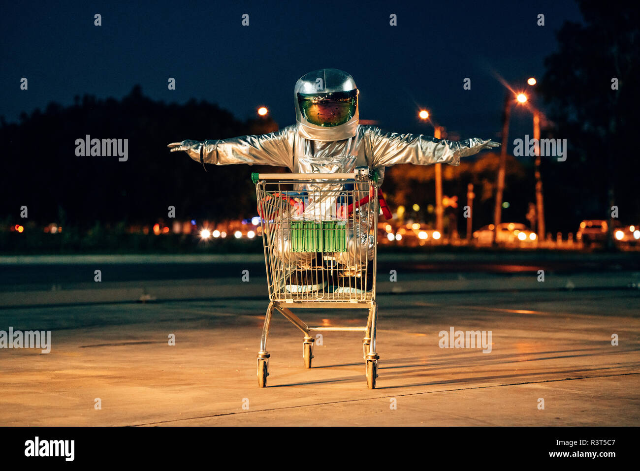 Spaceman in the city at night on parking lot inside shopping cart Stock Photo