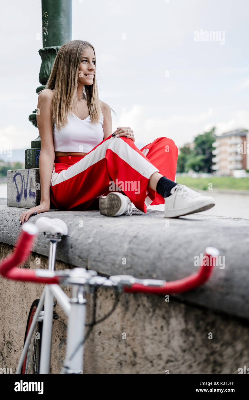 Smiling teenage girl sitting on a wall at the riverside next to bicycle Stock Photo