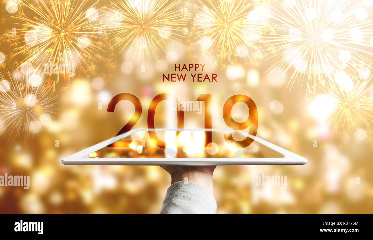 Happy New Year 2019, Hand holding digital tablet with luxury gold Bokeh fireworks background Stock Photo