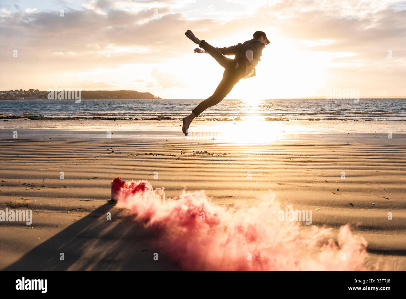 Man doing movement training at the beach with colorful smoke at sunset Stock Photo