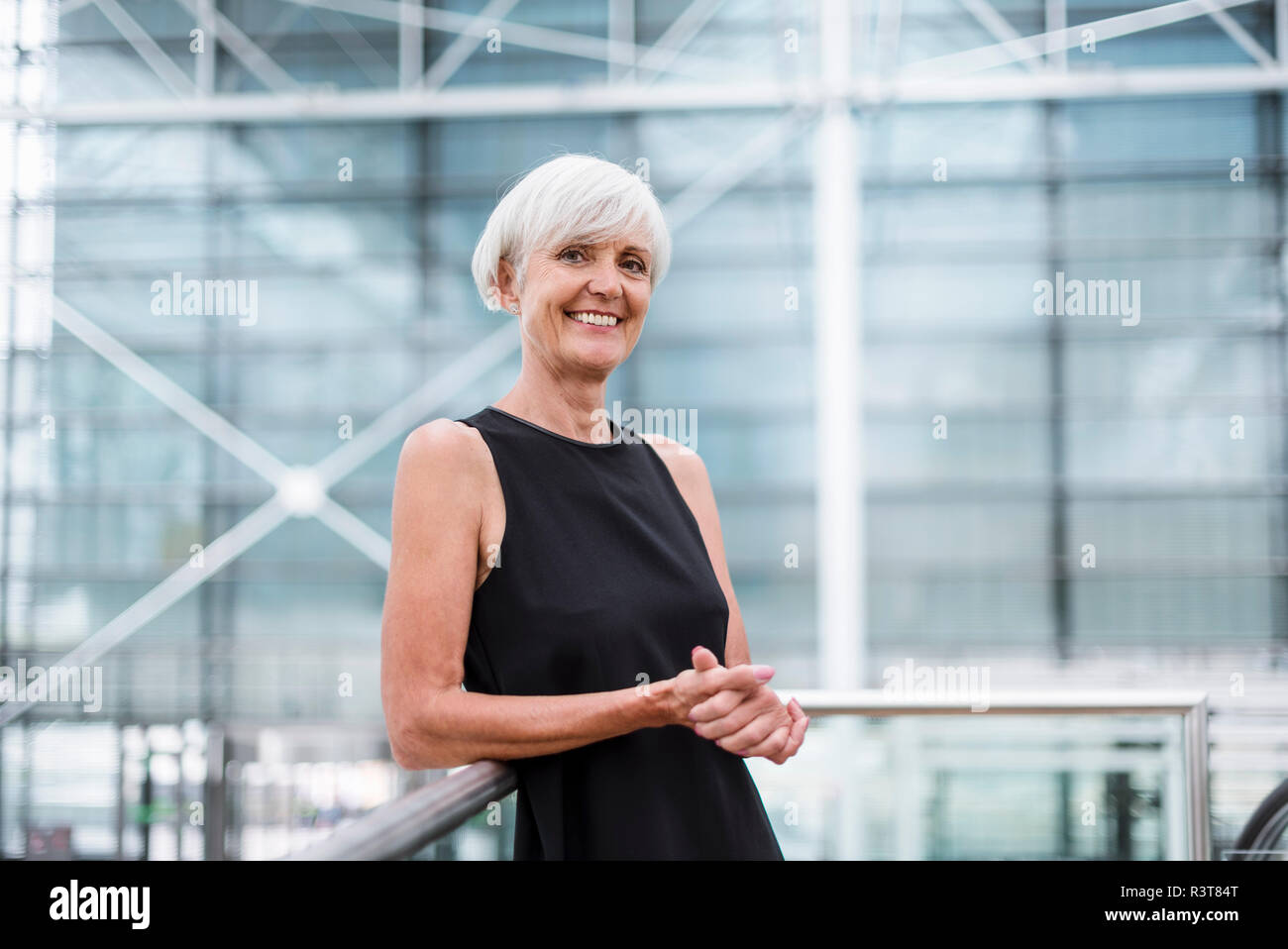 Portrait of smiling senior woman wearing black dress leaning against a railing Stock Photo