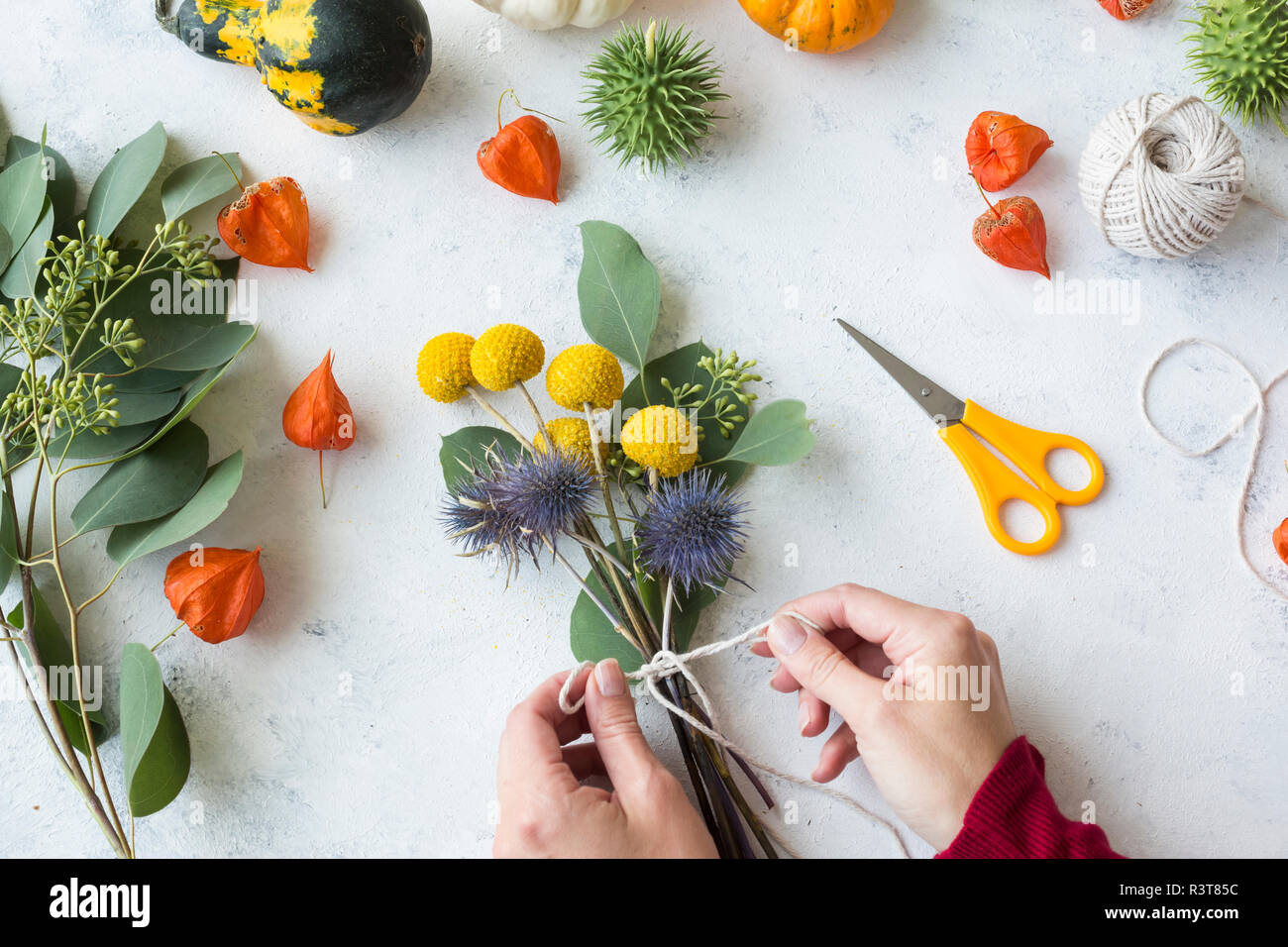 Autumnal decoration, ornamental pumpkins, woman's hand binding bunch of flowers Stock Photo