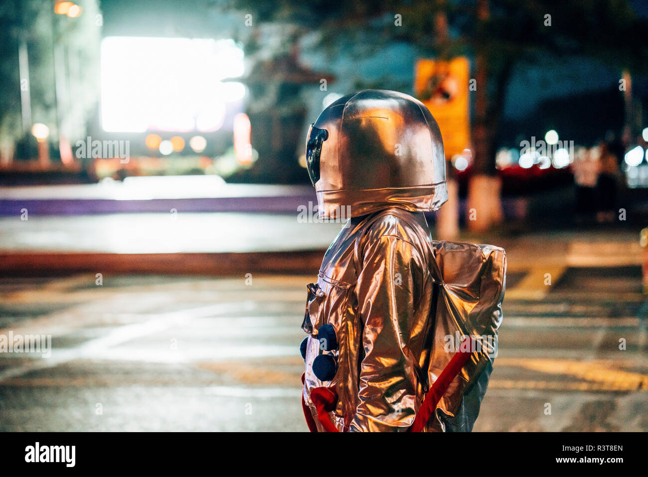 Spaceman on a street in the city at night attracted by shining projection screen Stock Photo
