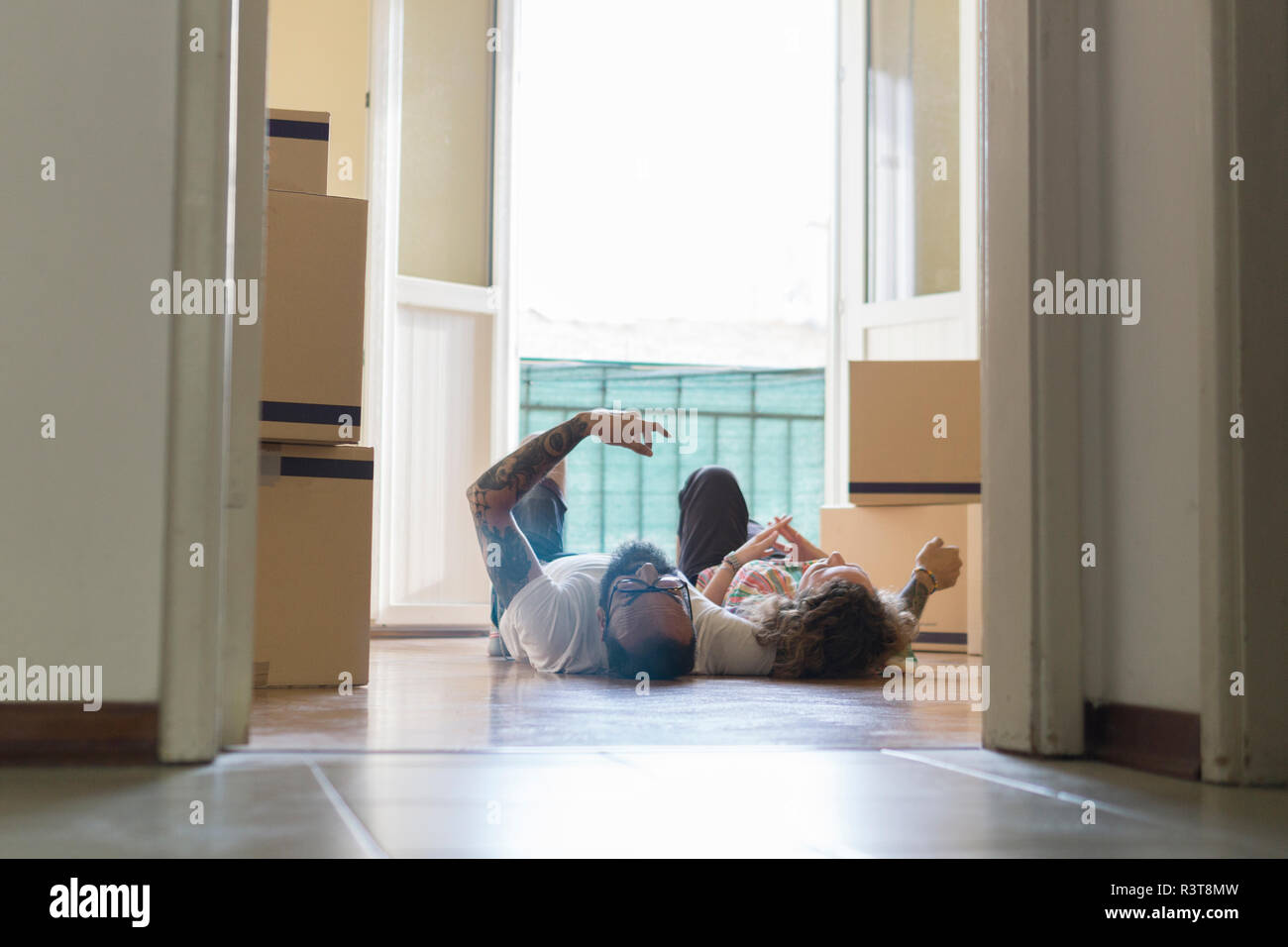 Couple lying side by side on the floor of new home in front of open balcony door Stock Photo