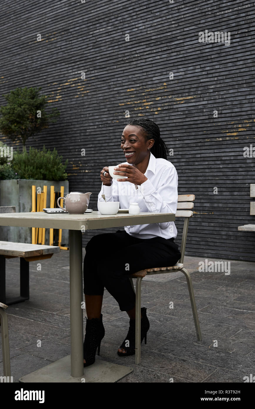 Laughing businesswoman sitting on  terrace of a coffee shop drinking tea Stock Photo