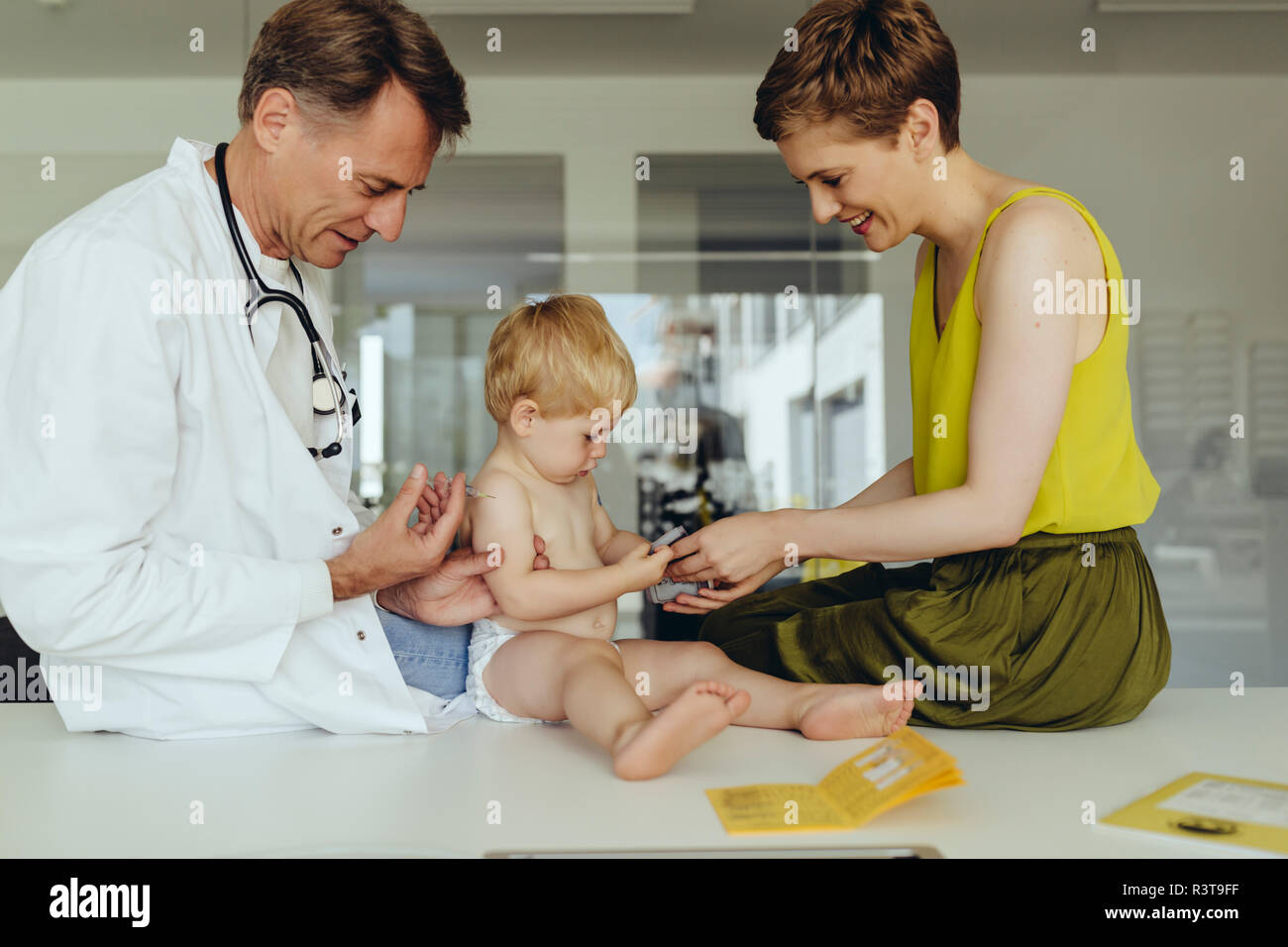 Pediatrician vaccinating toddler, injecting infant's arm, mother watching Stock Photo