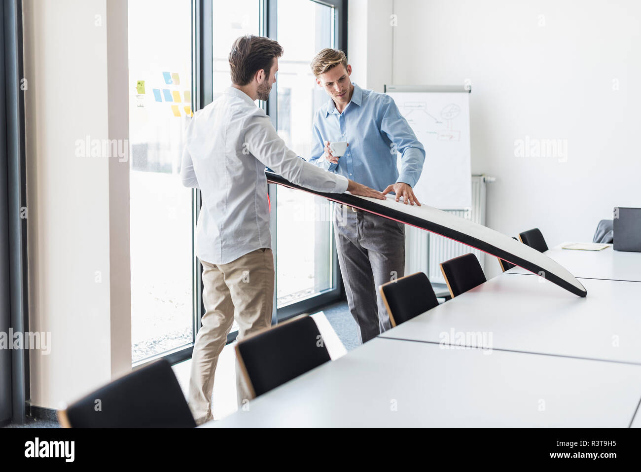 Two colleagues examining surfboard in office Stock Photo