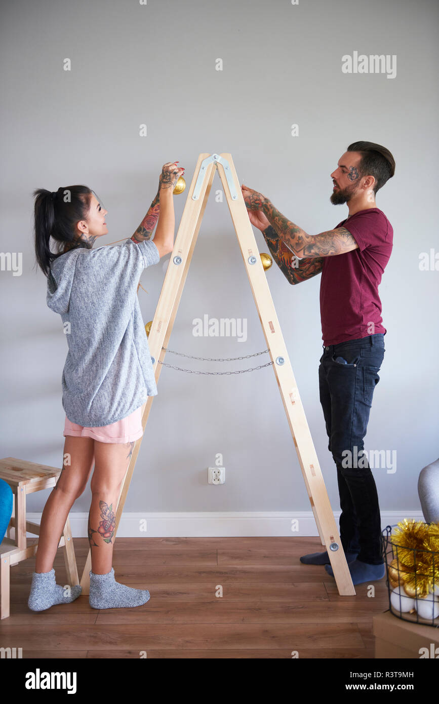 Modern couple decorating the home at Christmas time using ladder as Christmas tree Stock Photo