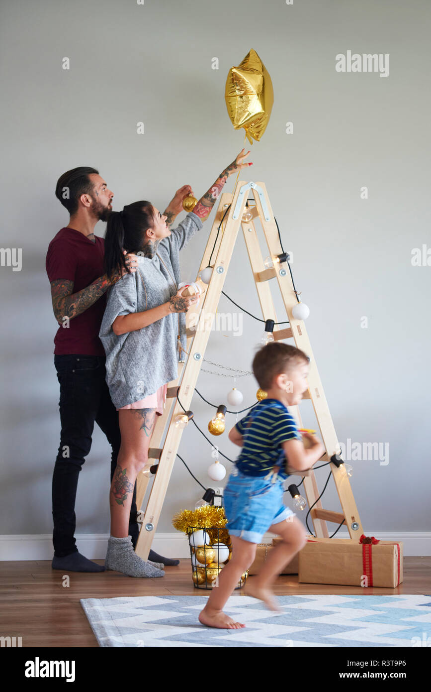 Modern family decorating the home at Christmas time using ladder as Christmas tree Stock Photo