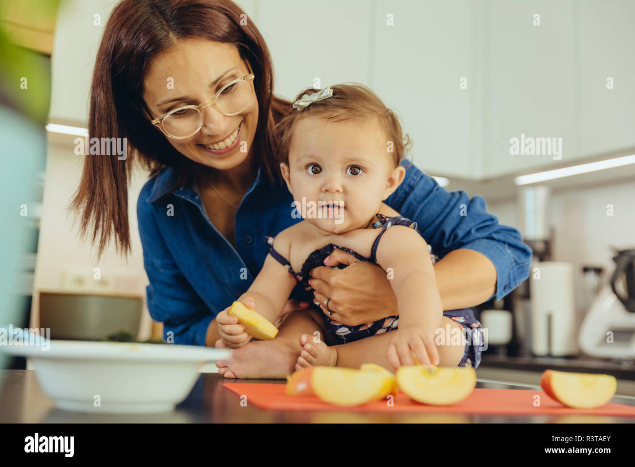 Mother and baby daughter eating apple chunks in kitchen Stock Photo