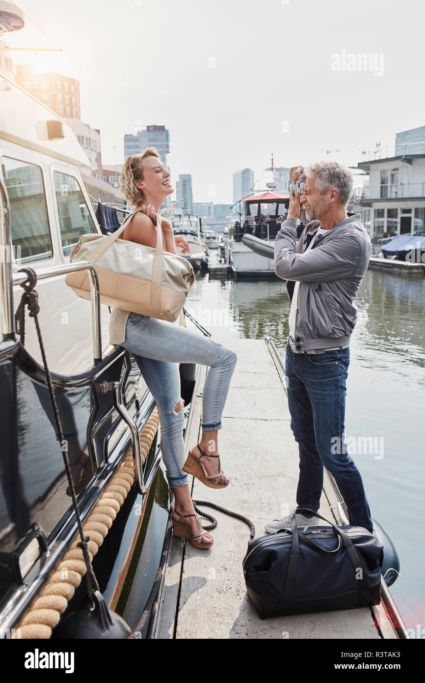 Older man taking picture of young woman on jetty next to yacht Stock Photo